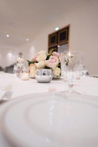 Centre de table avec bouquet de roses blanches et roses, bougies et vaisselle sur une table élégamment dressée.