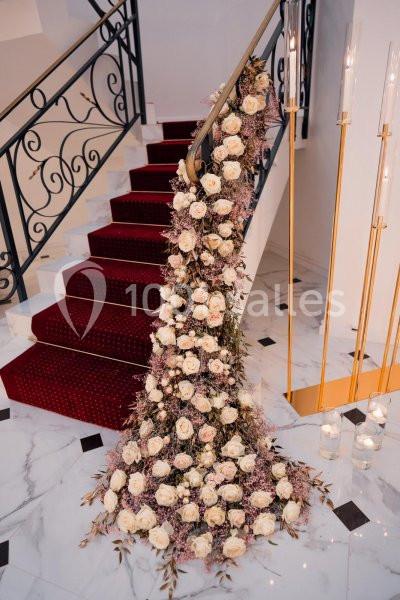 Décoration florale composée de roses blanches et roses, disposée le long d'une rampe d'escalier sur tapis rouge.