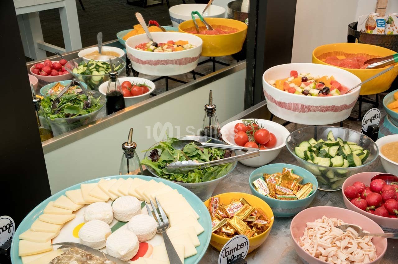 Buffet avec divers plats : salades, fromages, crudités, fruits et condiments, disposés sur une table.