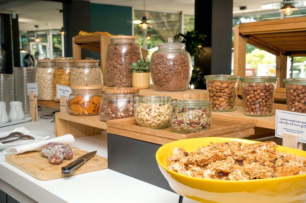 Buffet de petit-déjeuner avec céréales, fruits secs, noix et granola dans des bocaux en verre sur une table.