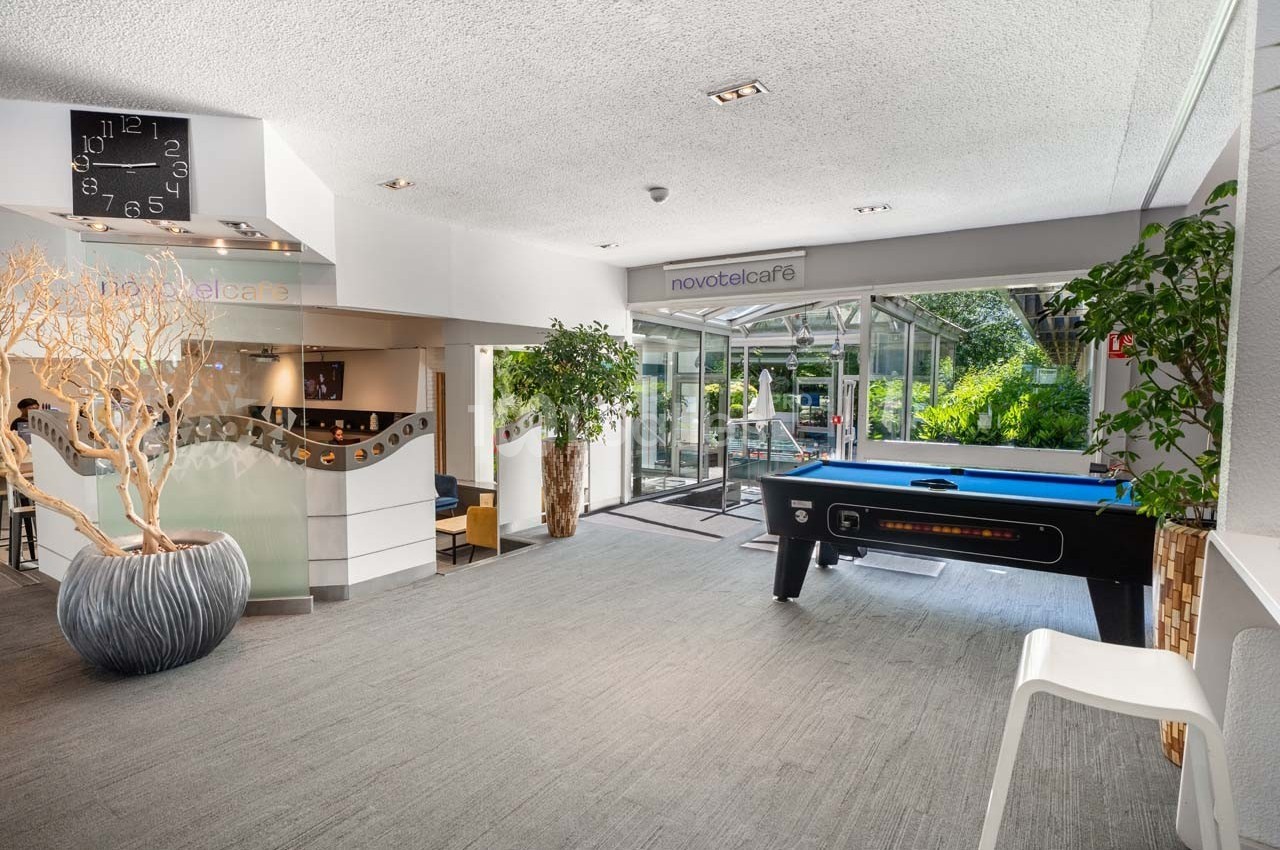 Espace lumineux avec un billard, des plantes et un coin café, donnant sur une terrasse extérieure verdoyante.