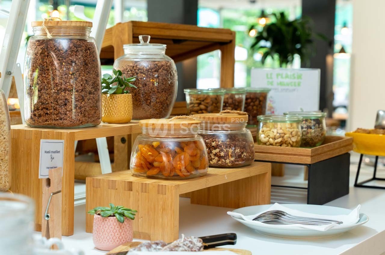 Buffet avec des bocaux en verre contenant des céréales, fruits secs et noix, disposés sur des supports en bois.