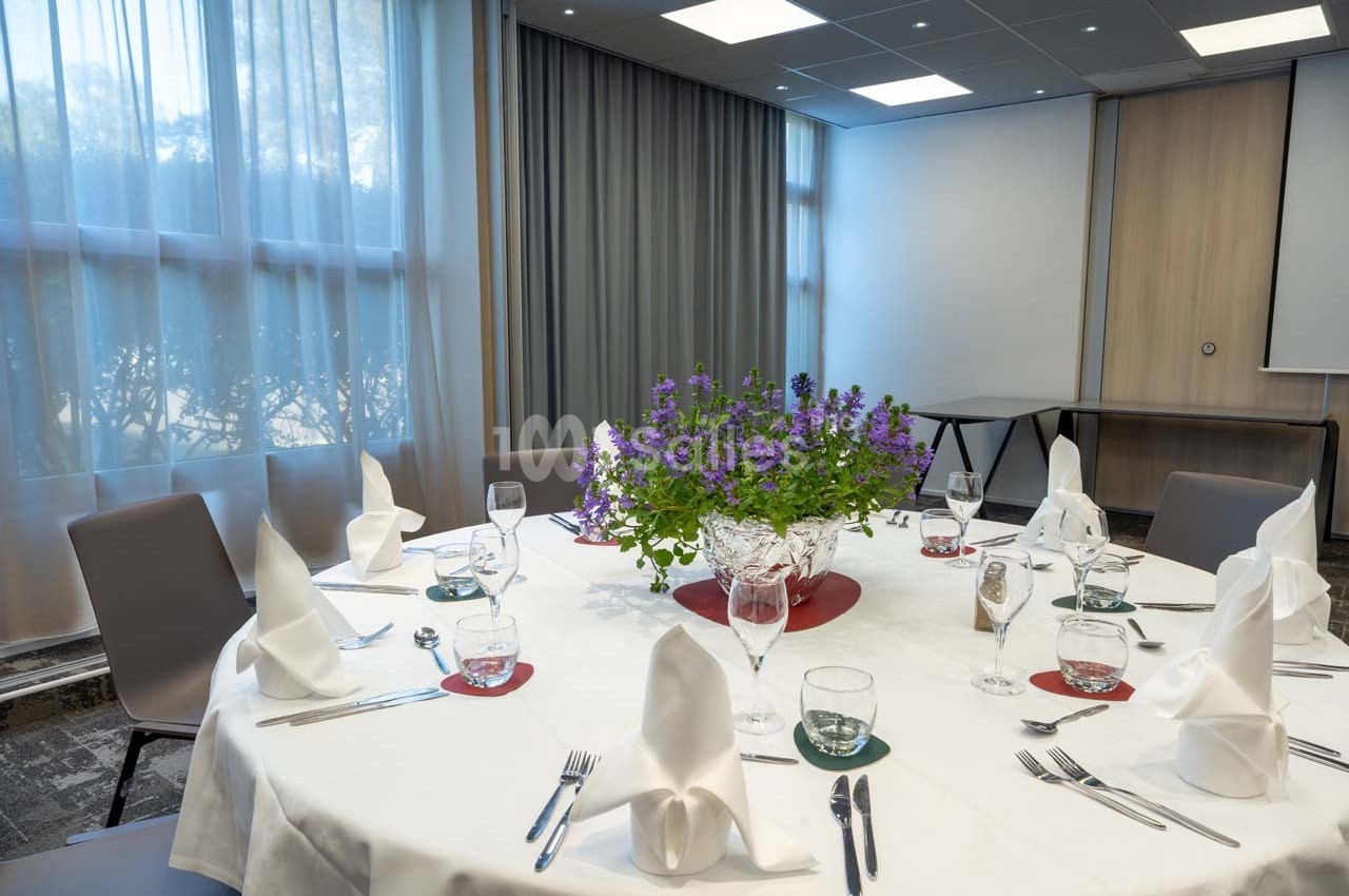 Table ronde dressée avec nappes blanches, serviettes pliées, verres et couverts, décorée d'un centre de table floral.