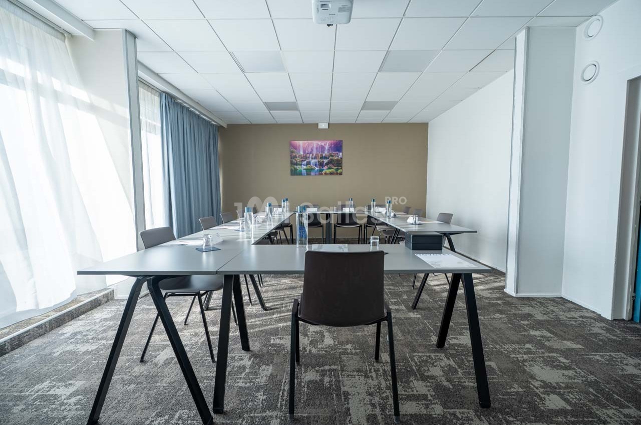 Salle de réunion lumineuse avec tables en triangle, chaises modernes, et un tableau mural coloré.