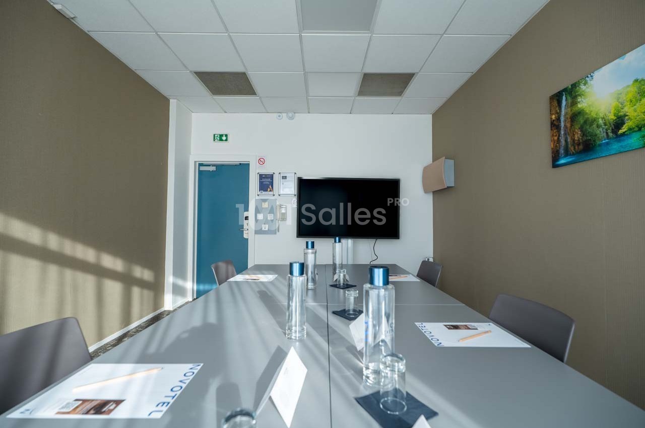 Salle de réunion lumineuse avec une grande table, des chaises, des bouteilles d'eau et un écran mural.