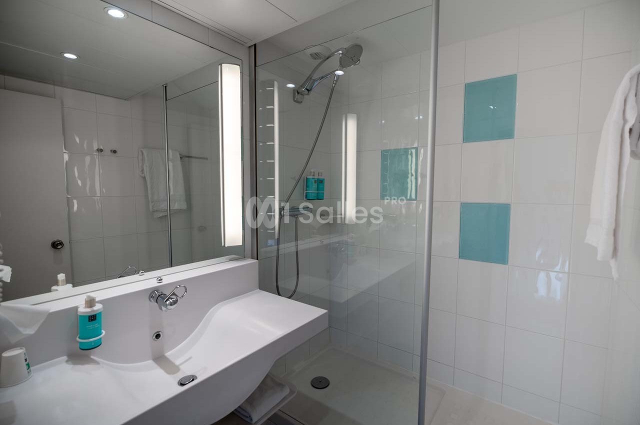 Salle de bain moderne avec douche à l'italienne, lavabo blanc, miroir éclairé et carreaux muraux bleus et blancs.