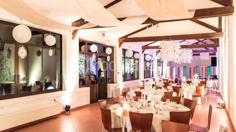 Salle de réception décorée avec des tables dressées, des suspensions lumineuses et des guirlandes en papier.