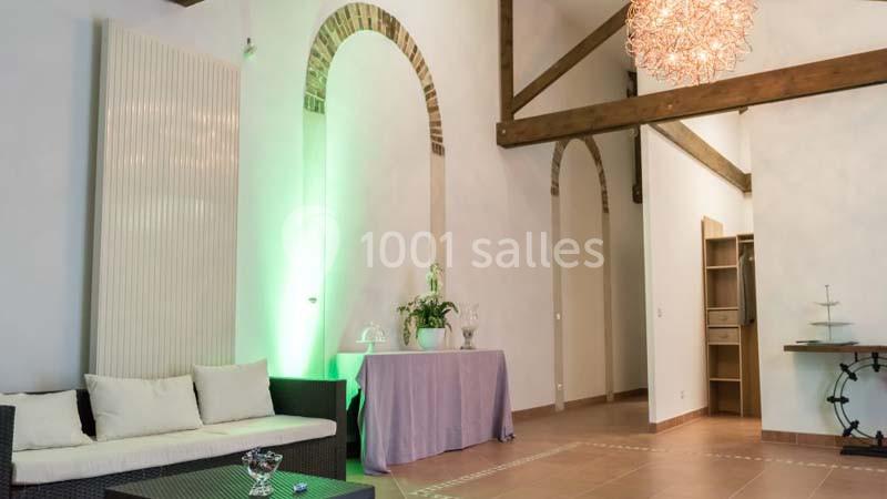 Salon lumineux avec canapé, table décorée, poutres apparentes, mur en briques et suspension design.