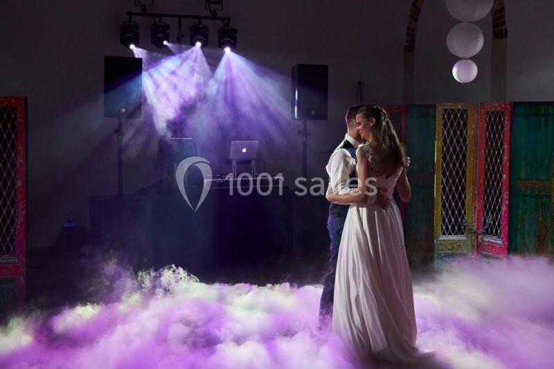 Un couple danse dans une salle sombre éclairée par des lumières colorées et entourée de fumée au sol.