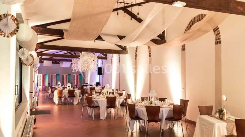 Salle de réception décorée avec des tables rondes dressées, des guirlandes suspendues et un éclairage chaleureux.