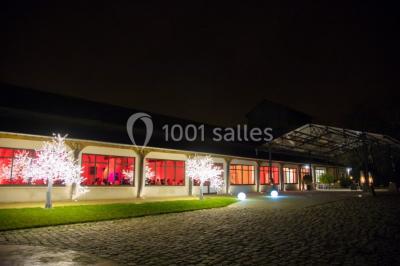 Salle de réunion avec une grande table rectangulaire, chaises noires, documents, bouteilles d'eau et écran de présentation.