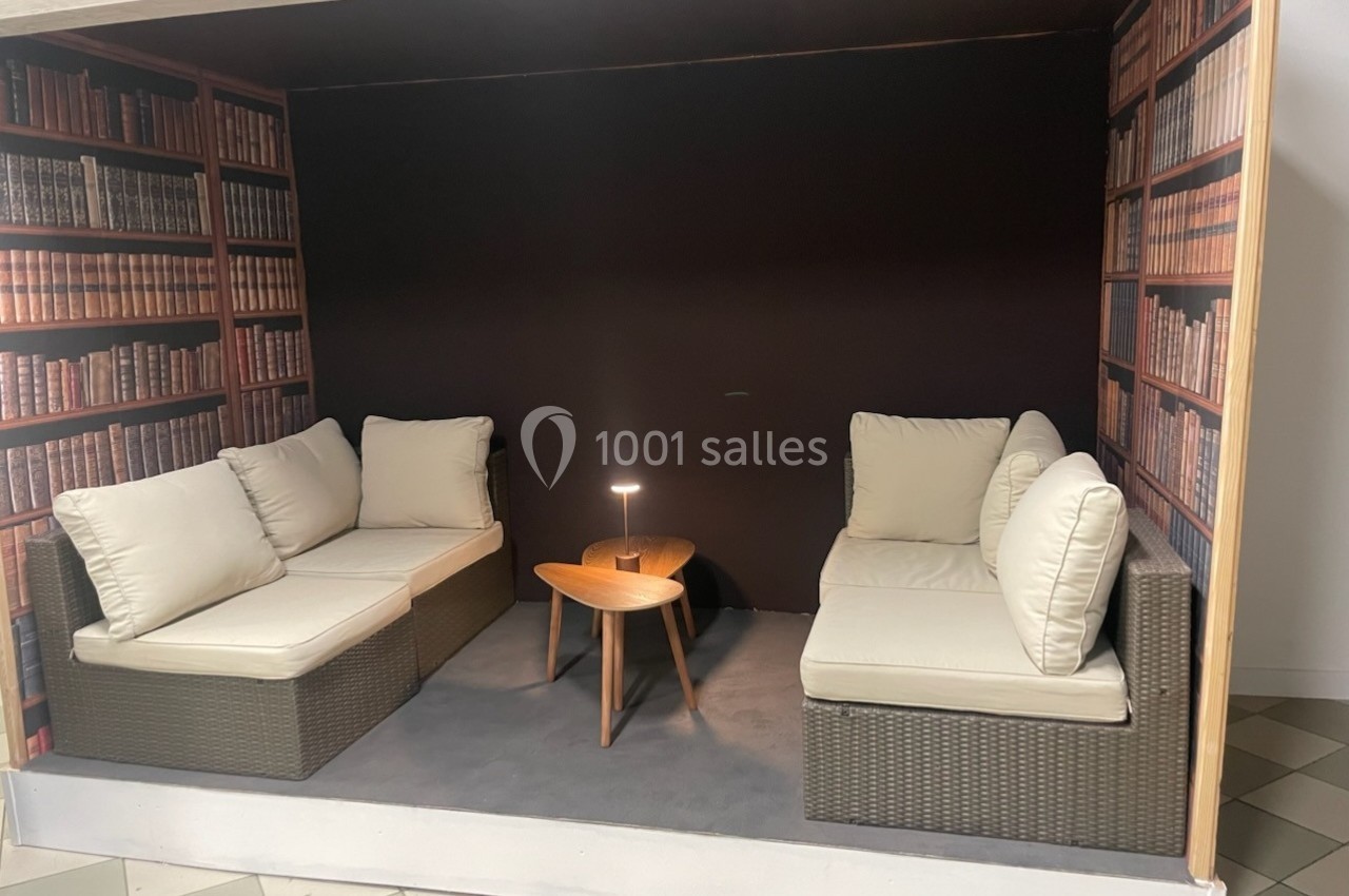 Deux canapés en rotin avec coussins beiges, une table basse en bois et une lampe, dans un espace décoré de faux rayonnages…