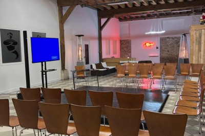 Salle de réunion avec une grande table rectangulaire, chaises noires, documents, bouteilles d'eau et écran de présentation.