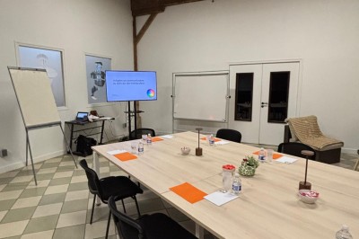 Salle de réunion avec une grande table rectangulaire, chaises noires, documents, bouteilles d'eau et écran de présentation.