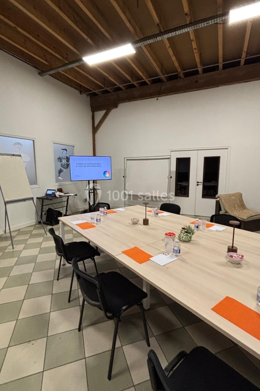 Salle de réunion avec table rectangulaire, chaises noires, écran de présentation, tableau blanc et plafond en bois apparent.