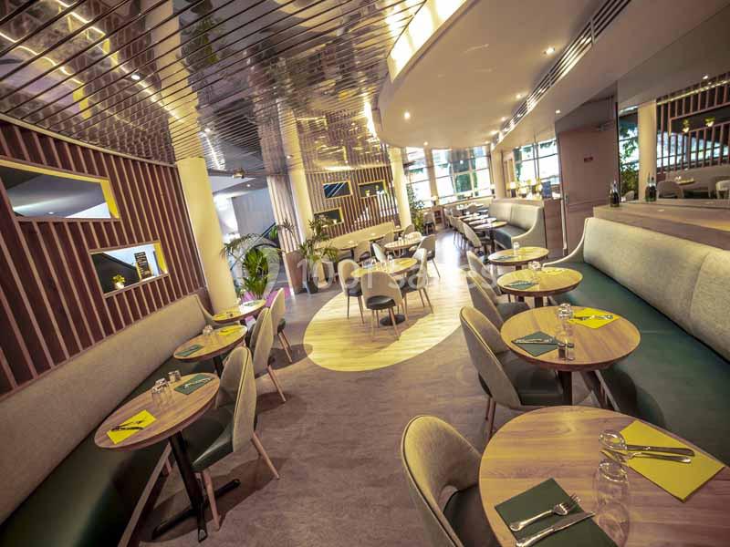 Salle de restaurant moderne avec tables en bois, chaises rembourrées et lumière naturelle entrant par de grandes fenêtres.