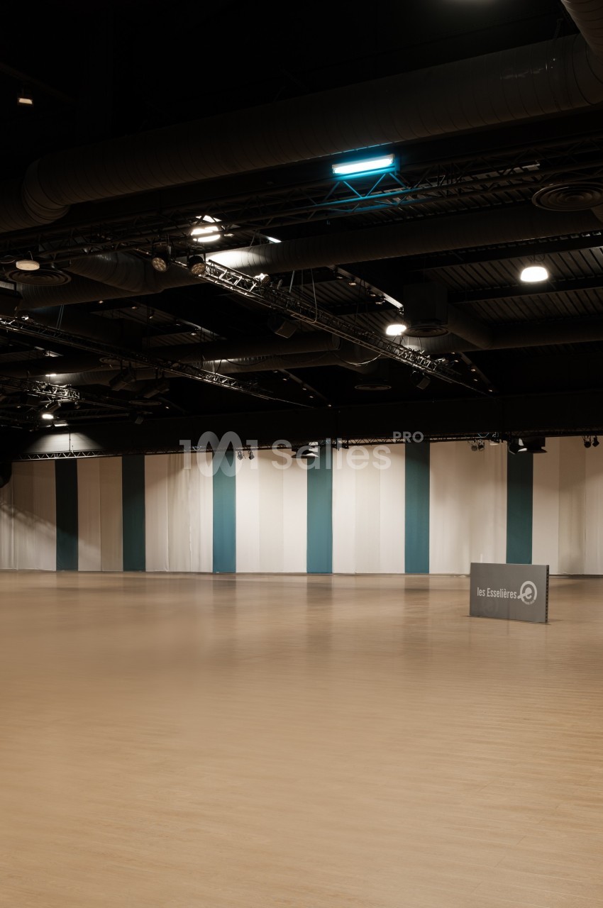 Salle vide avec parquet clair, murs rayés verticalement blanc et vert, et plafond noir avec éclairages suspendus.