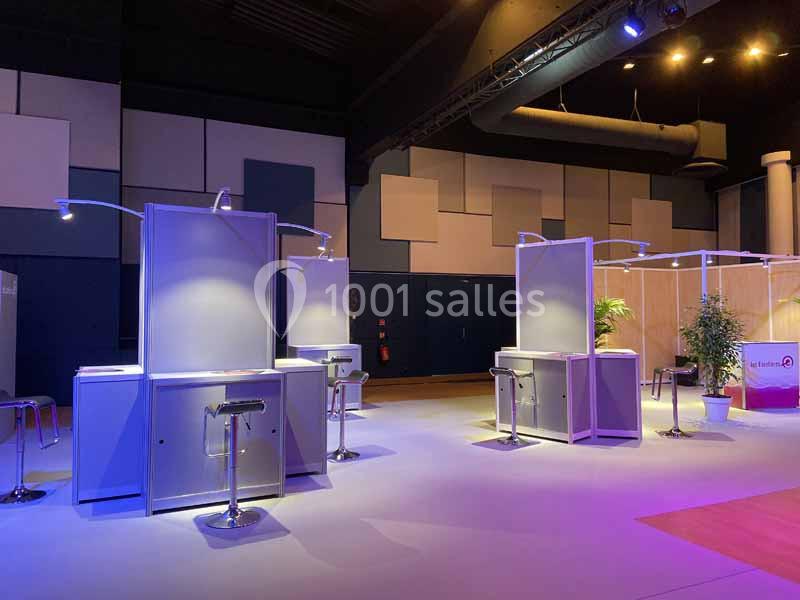 Stands d'exposition vides avec éclairage coloré dans une salle sombre, équipés de tabourets et de panneaux.