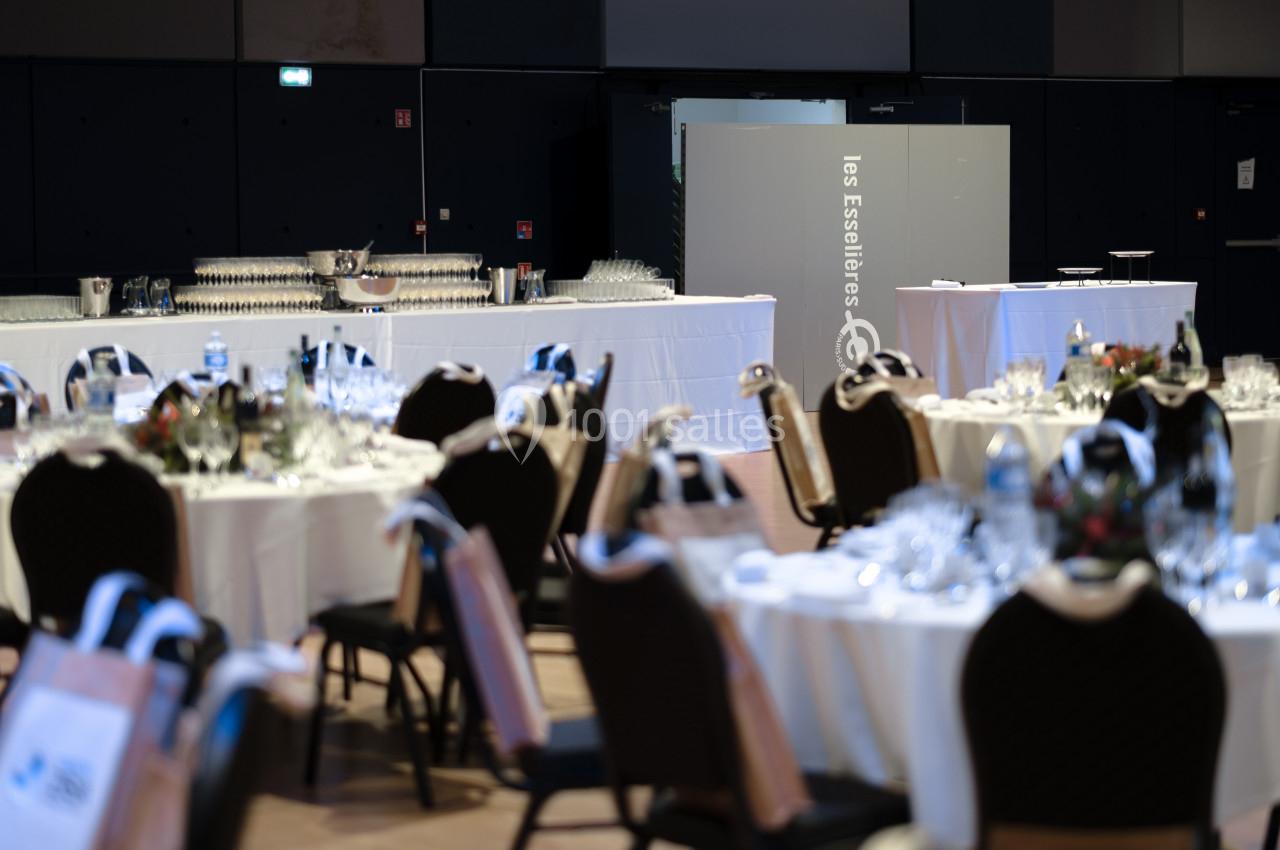 Salle de réception avec tables rondes dressées, verres et couverts, et un buffet en arrière-plan.