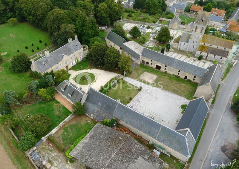 Vue aérienne d'un domaine historique avec bâtiments en pierre, cour centrale et église adjacente dans un cadre rural.