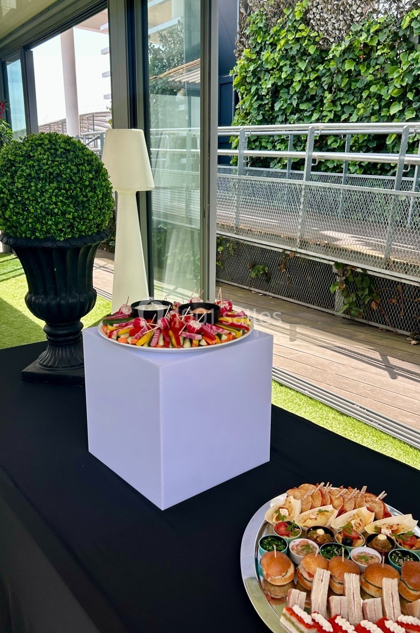 Plateau de fruits frais et assortiment de canapés disposés sur une table dans un espace extérieur lumineux.