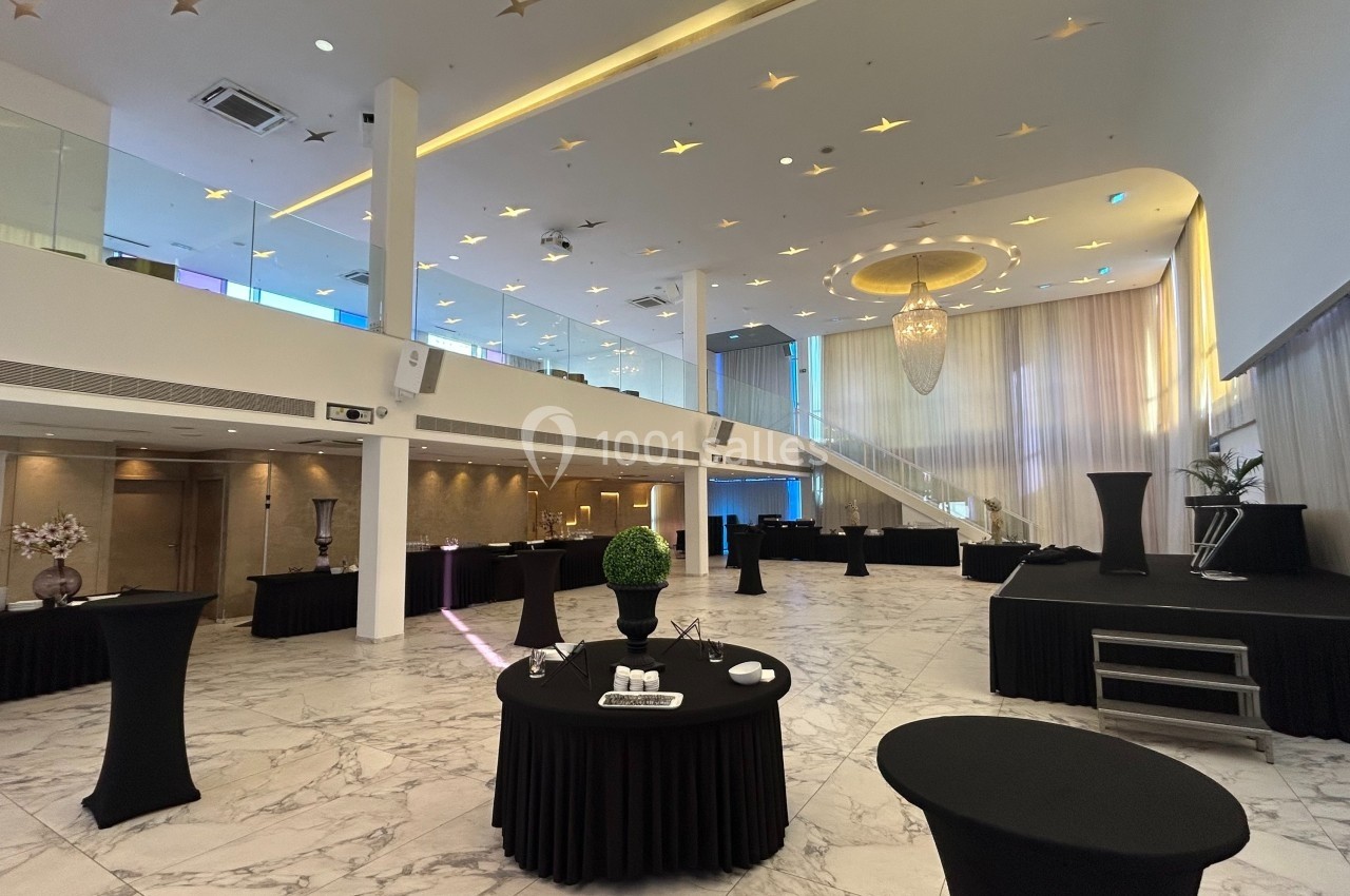 Salle de réception spacieuse avec mezzanine, tables hautes noires, sol en marbre et éclairage décoratif.