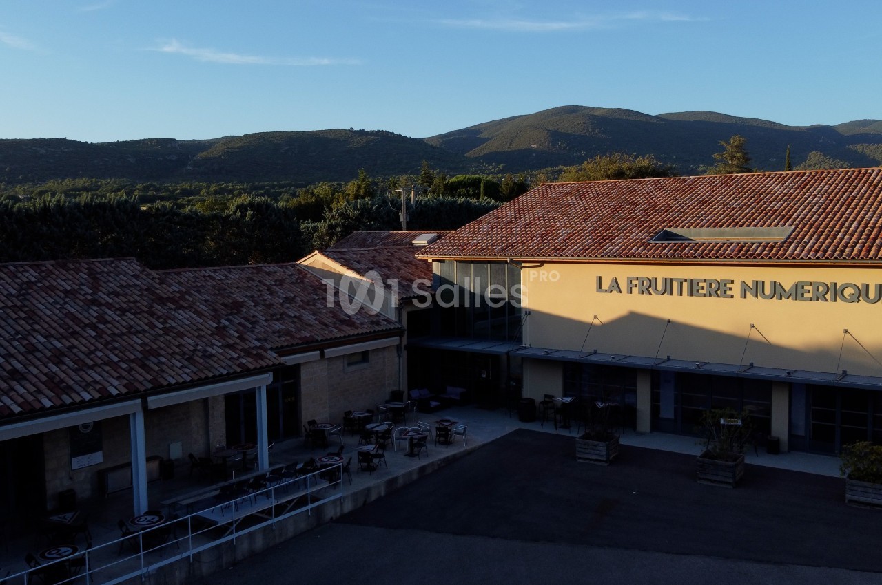 Bâtiment avec toit en tuiles, marqué ’La Fruitière Numérique’, entouré de montagnes et d'un ciel dégagé.