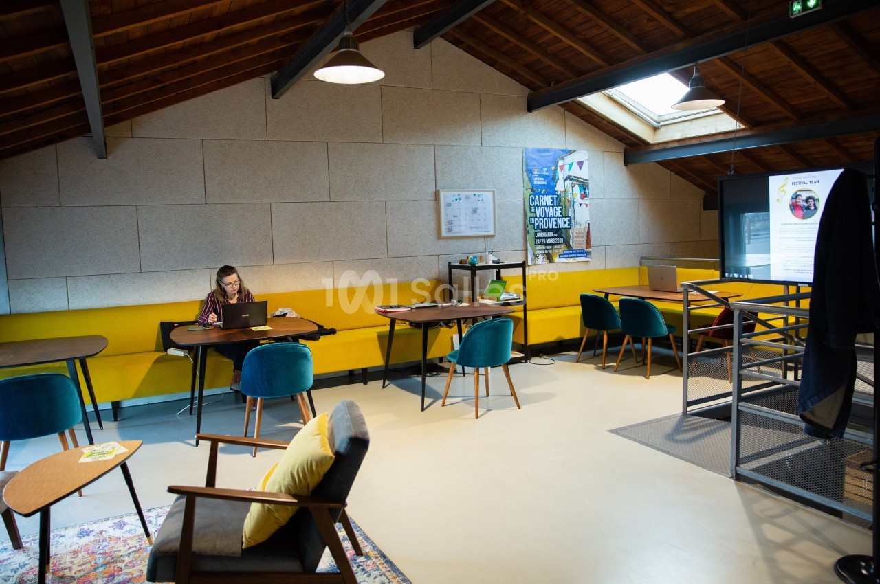 Espace de coworking lumineux avec mobilier coloré, une personne travaillant sur un ordinateur portable.