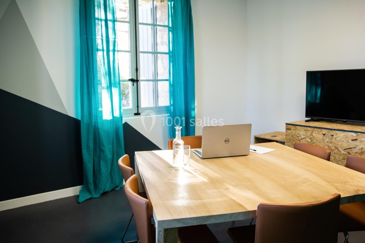 Salle de réunion lumineuse avec table en bois, chaises en cuir, rideaux turquoise, fenêtre et écran noir.