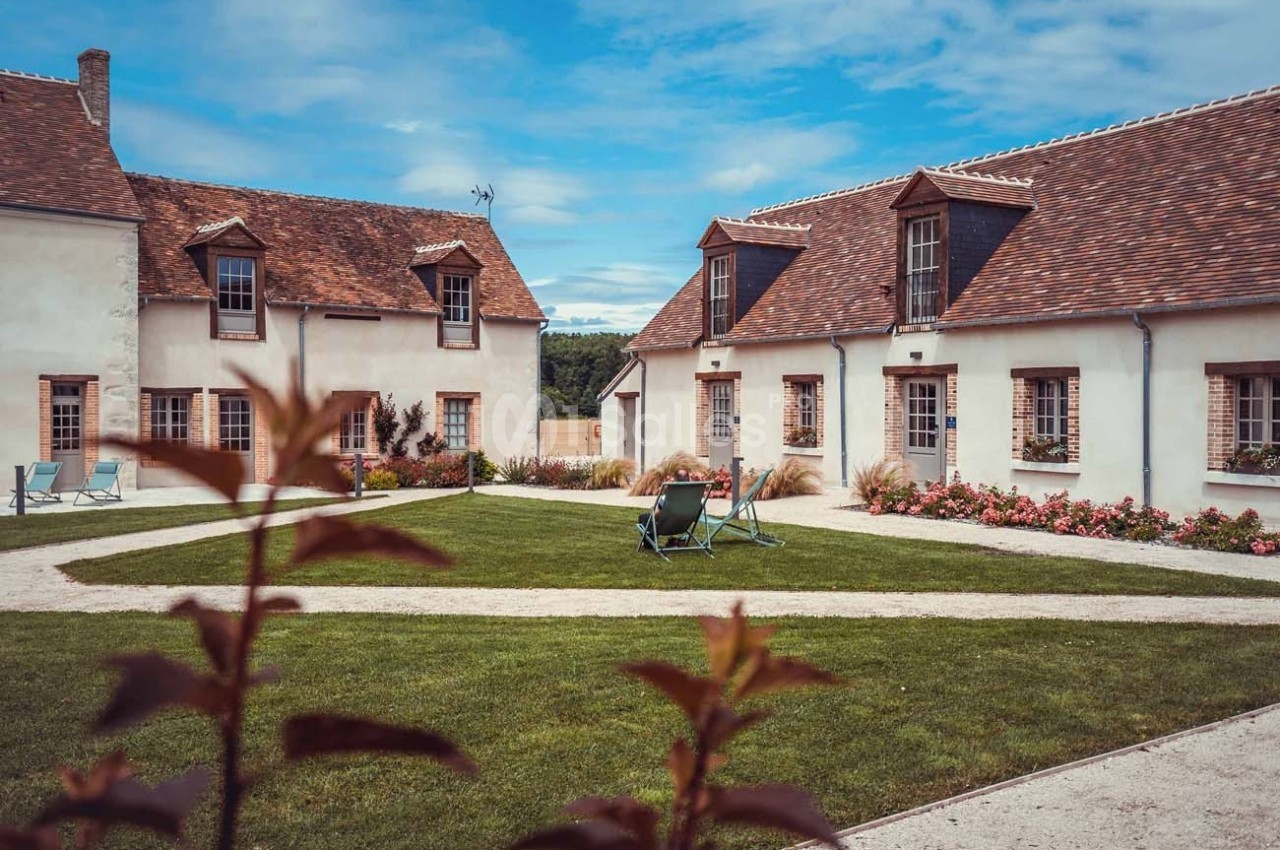 Cour intérieure avec pelouse, chaises longues et bâtiments aux façades blanches et toits en tuiles sous un ciel bleu.
