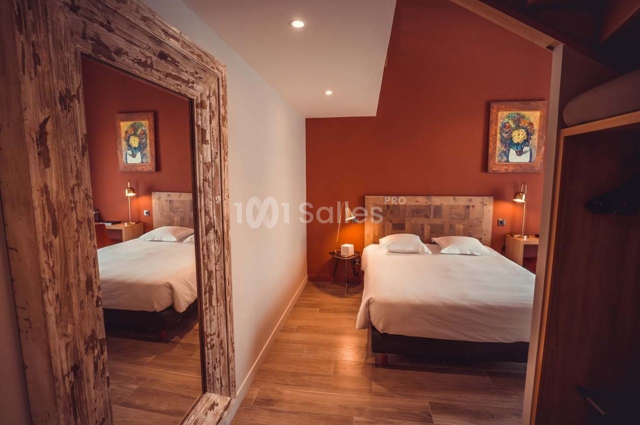 Chambre avec lit double, murs rouges, parquet, miroir encadré en bois et tableaux décoratifs.