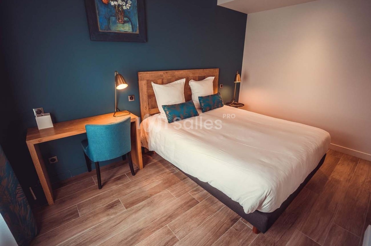 Chambre avec lit double, bureau en bois, chaise bleue et éclairage doux, décorée dans des tons bleus et neutres.