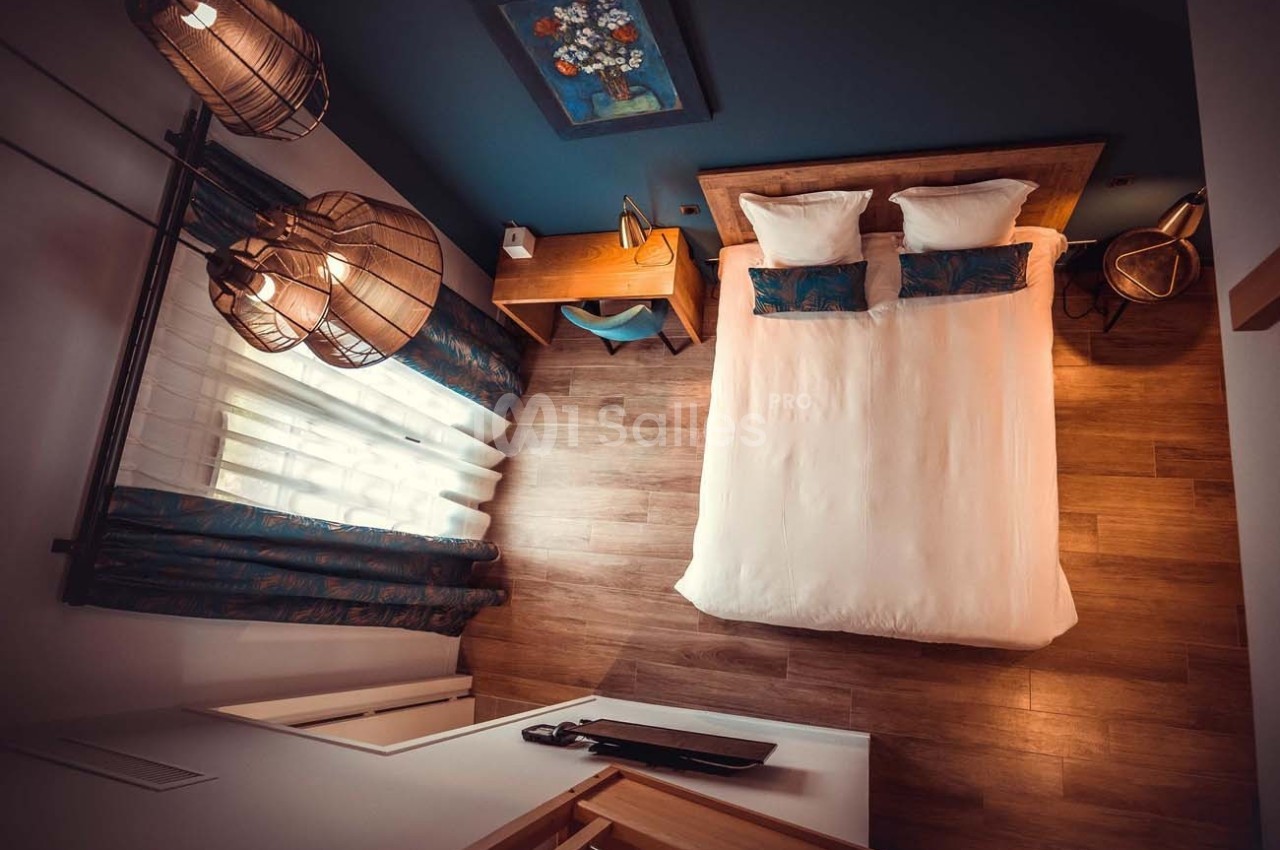 Vue aérienne d'une chambre avec un lit double, un bureau en bois, des luminaires suspendus et un sol en parquet.