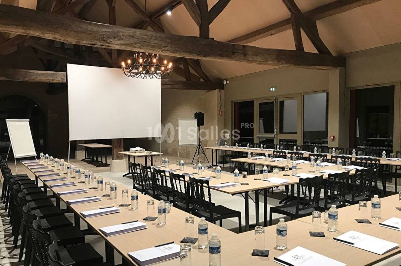 Salle de réunion avec de longues tables disposées en U, équipée d'un vidéoprojecteur, d'un paperboard et de bouteilles d'eau.