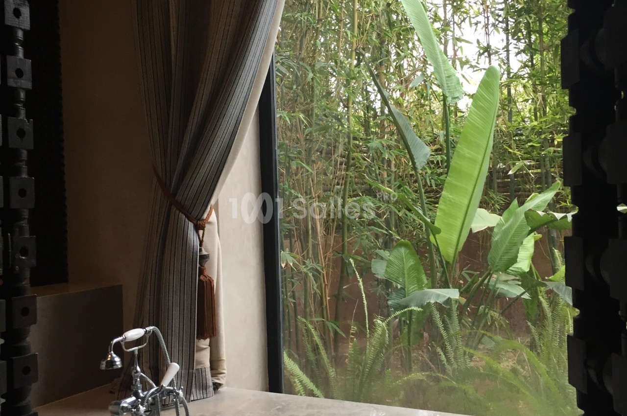Vue d'une salle de bain avec une baignoire près d'une grande fenêtre donnant sur un jardin tropical verdoyant.