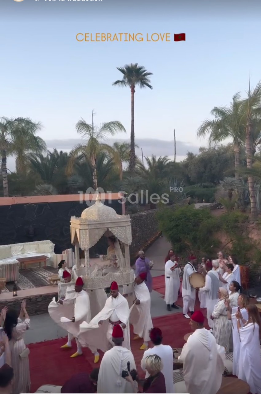 Un groupe de personnes en tenues traditionnelles danse autour d'un palanquin décoré, dans un cadre extérieur avec des…