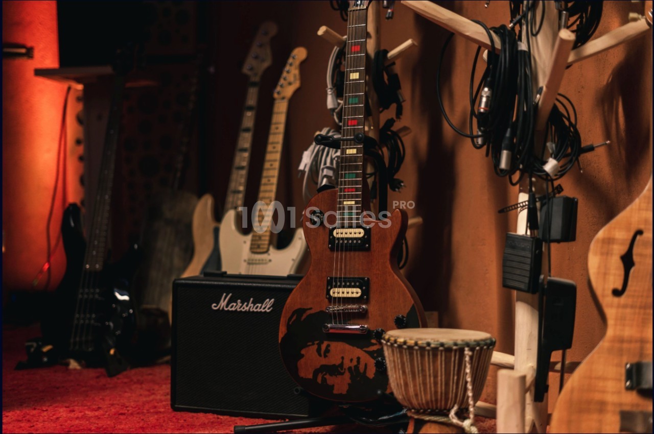 Guitares électriques et acoustiques posées près d'un ampli Marshall, avec un djembé et des câbles en arrière-plan.