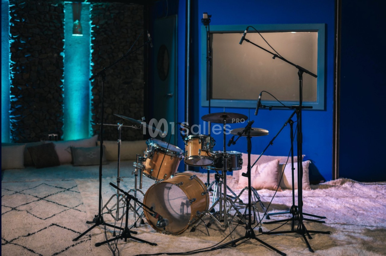 Batterie installée dans un studio d'enregistrement avec tapis au sol, murs bleus et éclairage tamisé.