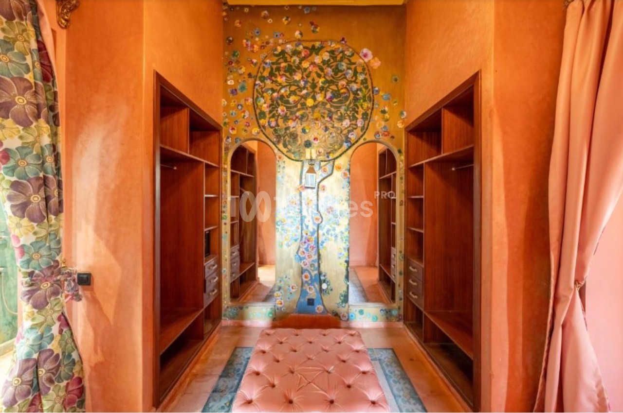 Dressing avec murs ornés d'une fresque d'arbre colorée, étagères en bois et pouf capitonné rose au centre.