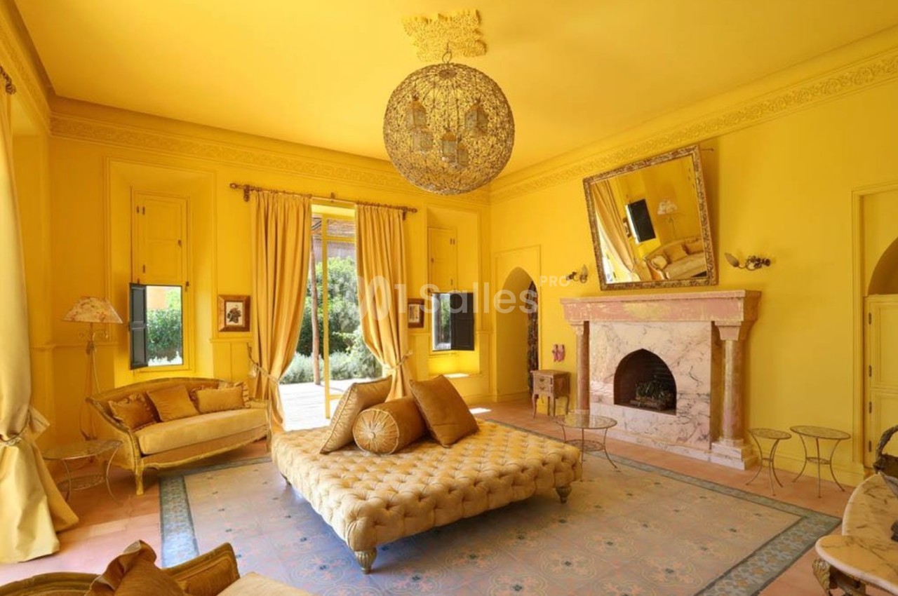 Salon lumineux aux murs jaunes, décoré avec des meubles élégants, un lustre imposant et une cheminée en marbre.