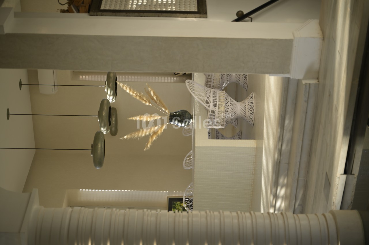 Espace intérieur lumineux avec des meubles en métal blanc, des suspensions modernes et un vase décoratif avec des pampas.