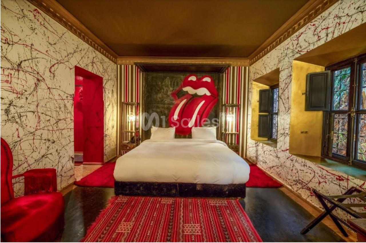 Chambre décorée avec des motifs artistiques, lit central, mur orné d'une grande langue rouge emblématique.