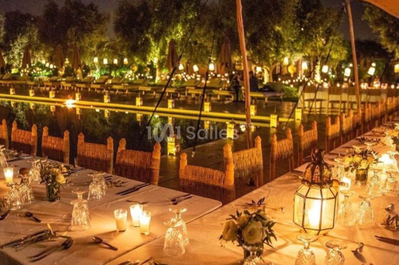 Tables élégamment dressées avec bougies et lanternes, face à un jardin illuminé et un plan d'eau, de nuit.
