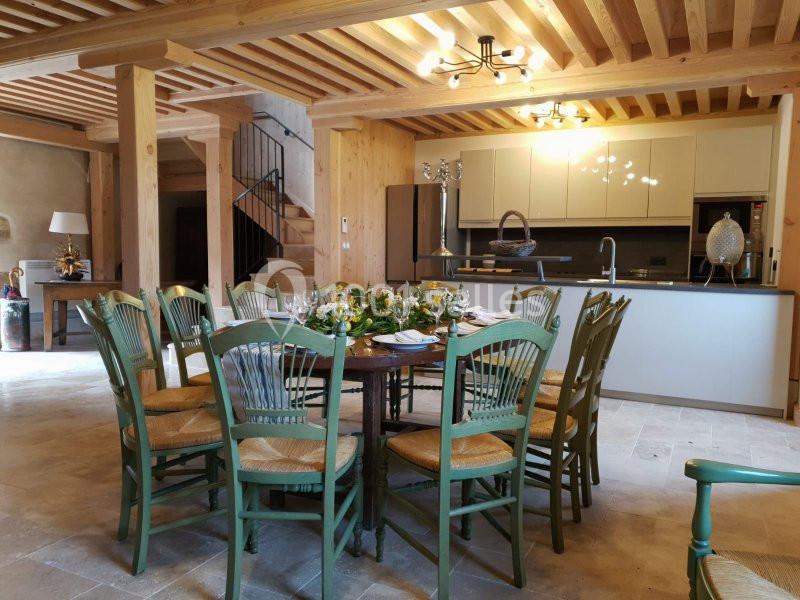 Location salle Maligny (Côte-d'Or) - Domaine du Grand Nanteux #24 Salle à manger lumineuse avec table ronde entourée de chaises vertes, cuisine ouverte et poutres apparentes en bois.