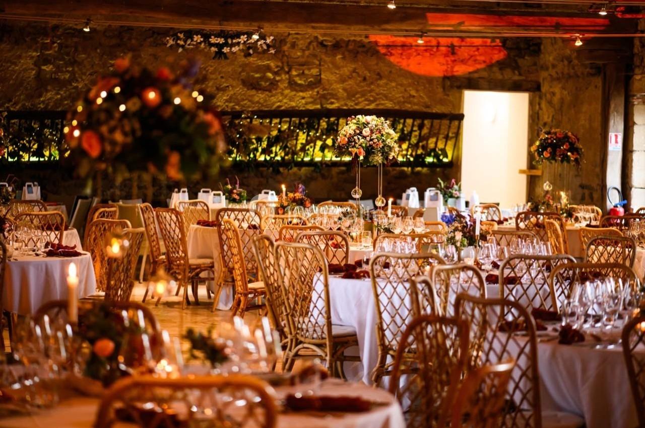 Location salle Maligny (Côte-d'Or) - Domaine du Grand Nanteux #2 Salle de réception décorée avec des tables rondes, nappes blanches, chaises en rotin et arrangements floraux colorés.