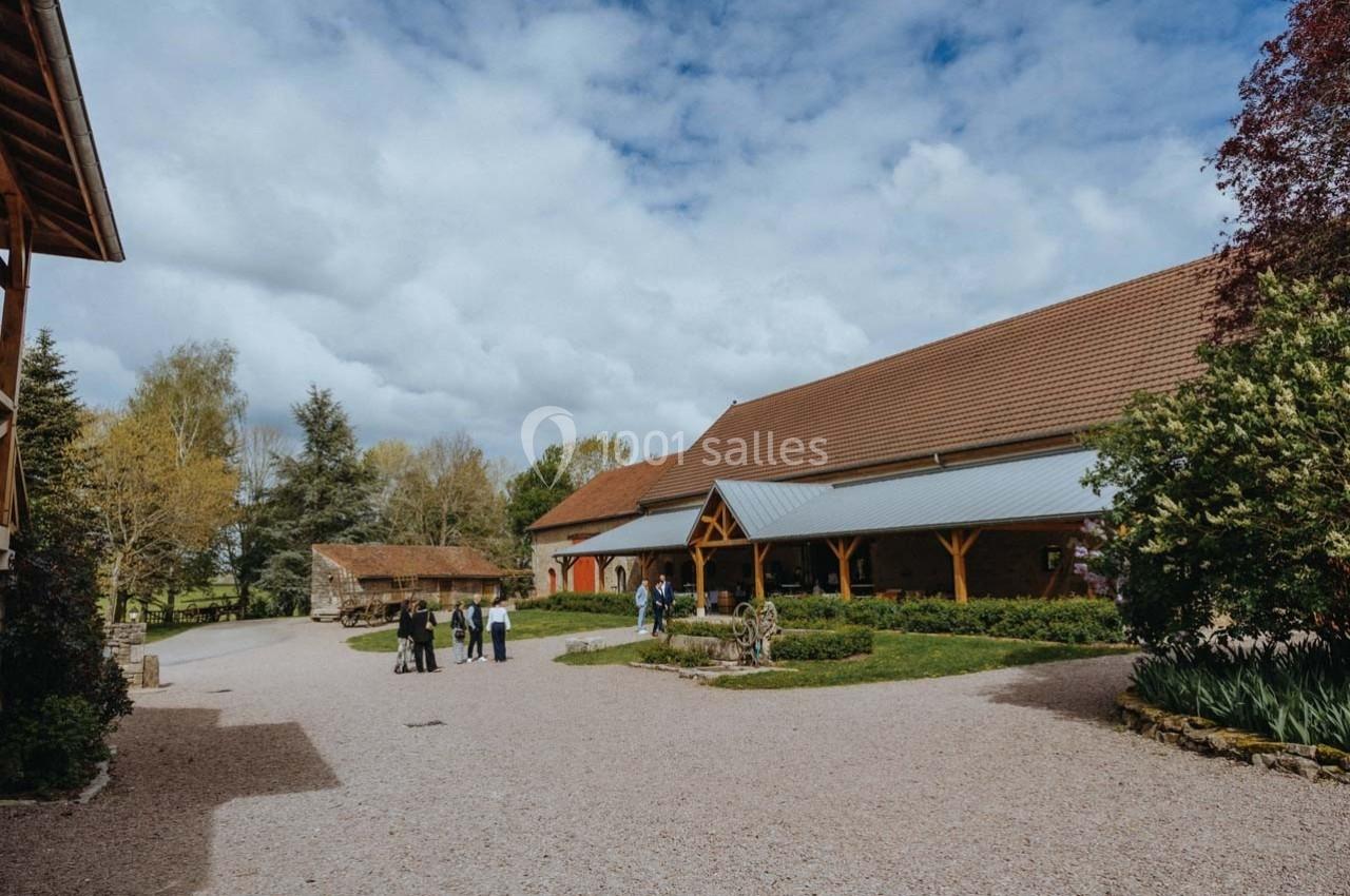 Location salle Maligny (Côte-d'Or) - Domaine du Grand Nanteux #13 Cour d'une ferme avec bâtiments en pierre et en bois, quelques arbres, et un petit groupe de personnes discutant.