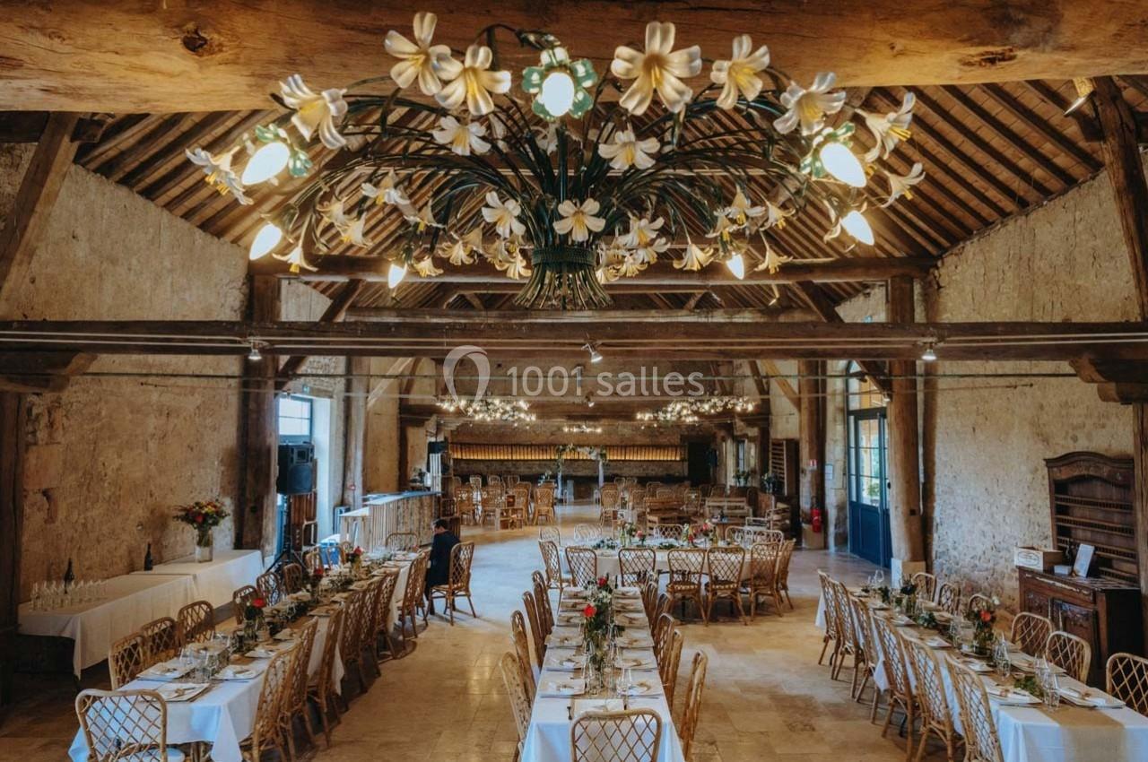 Location salle Maligny (Côte-d'Or) - Domaine du Grand Nanteux #7 Salle de réception rustique avec tables dressées, chaises en bois et lustres ornés de fleurs blanches.