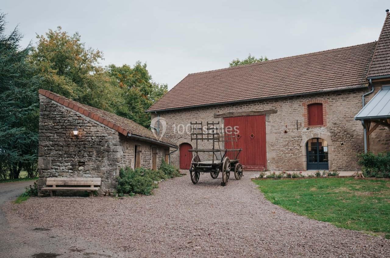 Location salle Maligny (Côte-d'Or) - Domaine du Grand Nanteux #32 Cour d'une ferme avec une grange en pierre, une charrette en bois et un bâtiment annexe sous un ciel couvert.