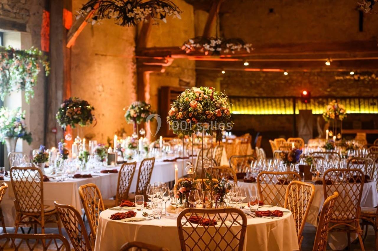 Location salle Maligny (Côte-d'Or) - Domaine du Grand Nanteux #11 Salle de réception décorée avec des tables rondes, des chaises en bois et des centres de table fleuris sous un éclairage…