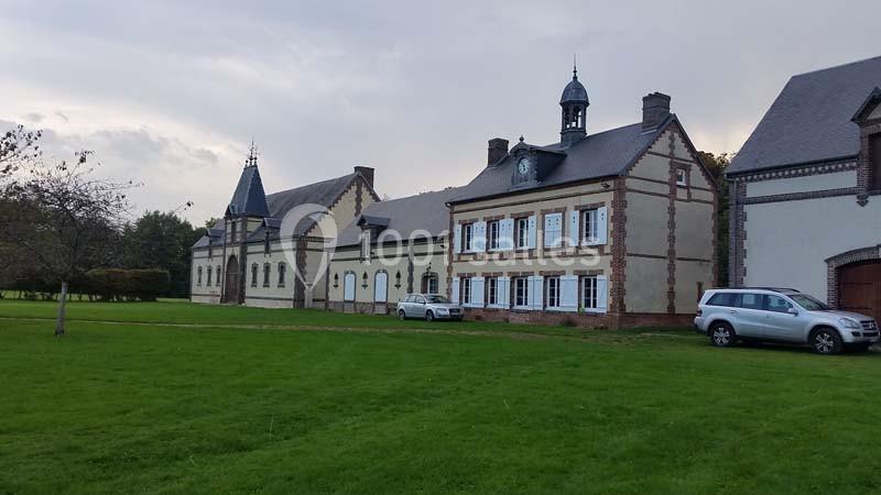 Location salle Sylvains-les-Moulins (Eure) - Domaine de Coulonge #14 Bâtiment ancien en briques et pierre avec des toits en ardoise, entouré d'une pelouse et de quelques arbres.